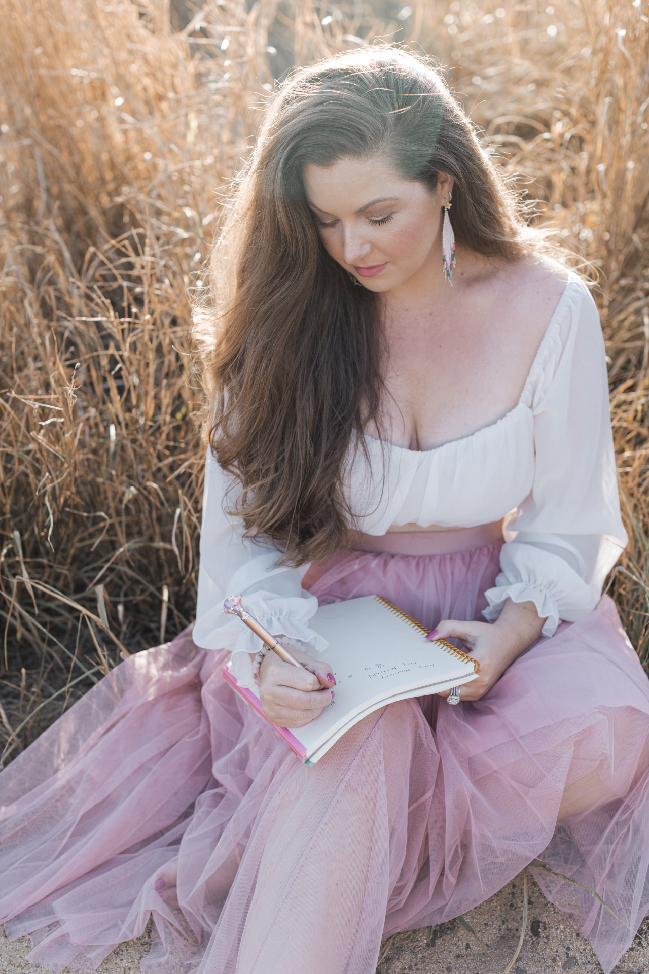 Amy McNally journaling in golden grass, wearing a white top and blush tulle skirt